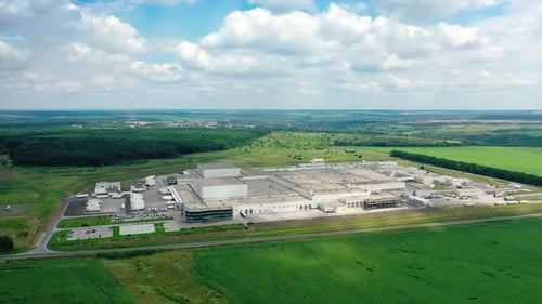 Large factory outside the city. Industrial plant on green fields and forests background.