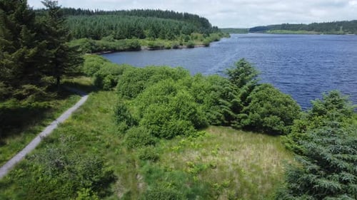Idyllic blue water reservoir lake woodland hiking walk aerial view low dolly right over trees