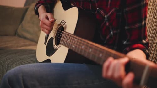 Close Up Woman Hands Playing Acoustic Guitar on a Couch in Cozy Living Room During Evening Hours