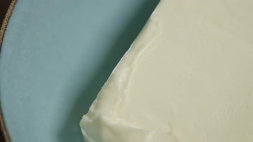Close-up shot of a fresh block of butter lying in a ceramic bowl. Panning shot. No face, studio.