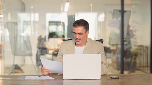 Happy Middle Aged Business Man Checking Documents Using Laptop in Office