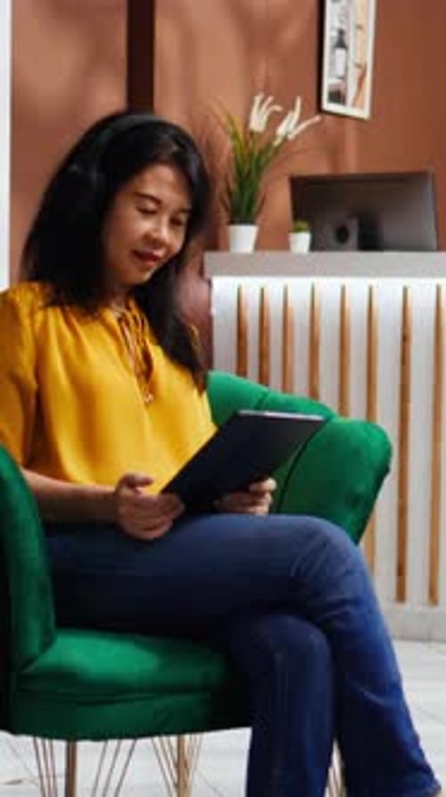 Vertical Video Asian Woman Checking Webpages on Tablet in Hotel Lobby