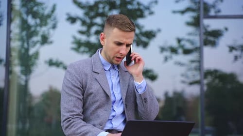 Focused Man Working on Laptop Talking on Phone