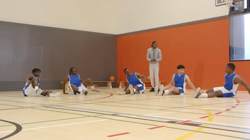 Basketball players stretching on court with coach supervising training session