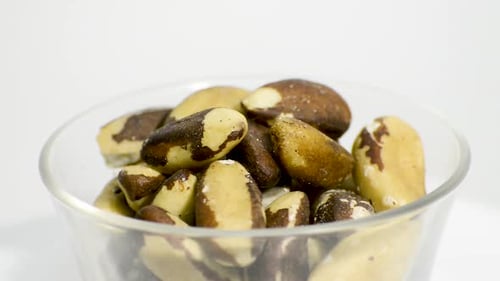 Transparent glass bowl with Brazil nuts rotating on a white background. Flat plane. High angle shot