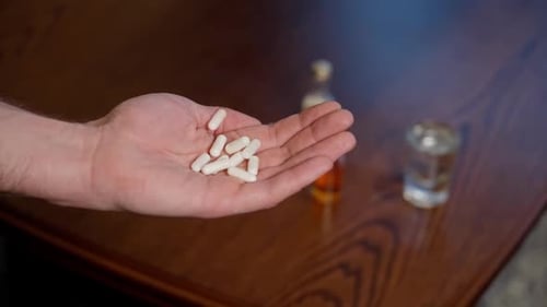 Hand Holding Pills With Alcohol on Table