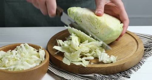 Woman cutting fresh cabbage at white wooden table, closeup