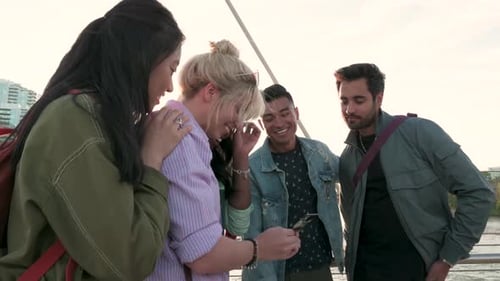 Adult Friends Using Smart Phone On Sunny Urban Bridge