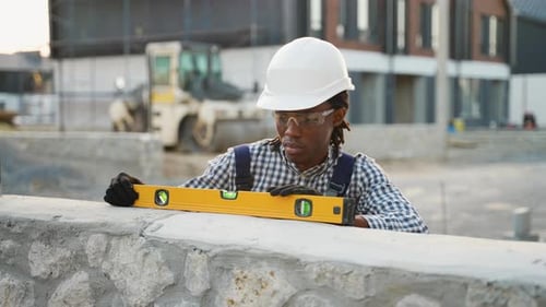 Afroamerikanischer Bauarbeiter benutzt Wasserwaage an einer Wand