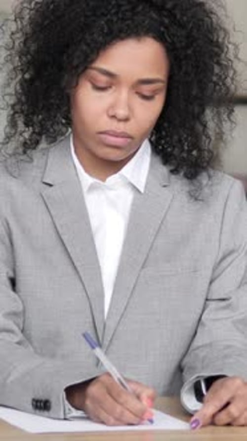 Young Woman Writes at Desk in Business Attire