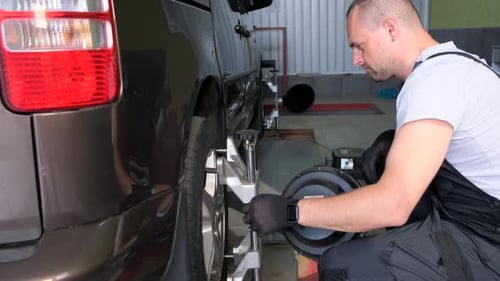 Man Fixing Tire on Van in Garage Adjusting Automotive Equipment