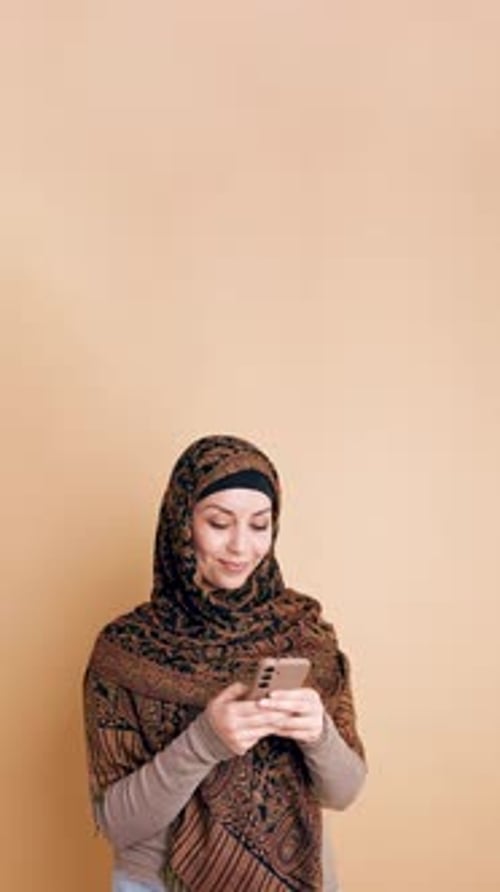 Young Muslim Woman Wearing a Hijab Texting on Her Smartphone Vertical