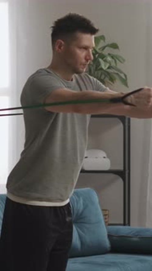 Focused Man Performing Resistance Band Workout at Home in Modern Living Room Strengthening Upper
