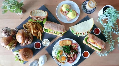 Cafe latte pushed into frame next to brunch flat lay with sandwiches, burger and chips.