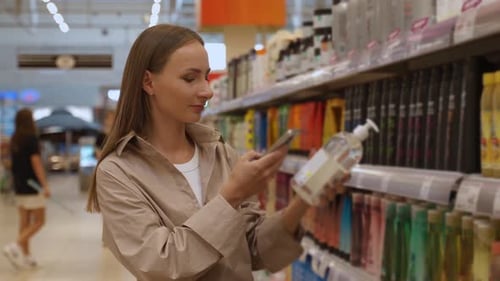 A Woman in a Beige Shirt Stands in the Aisle of a Grocery Store She Looks Through the Shelves of