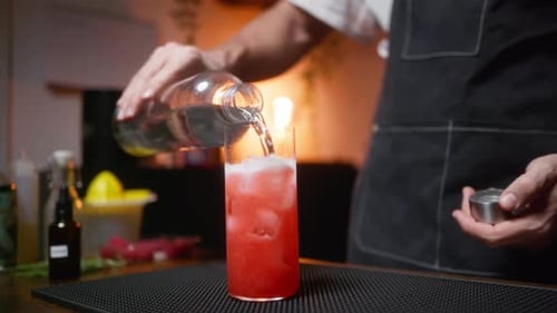 Bartender pouring soda into a vibrant cocktail in a cozy setting. Perfect for nightlife or bar scene