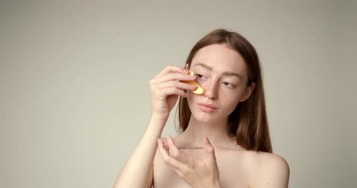 Young Woman Applies Gold Cosmetic Eye Patch
