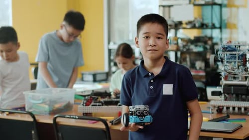 Asiatischer Junge hält einen handgefertigten Roboter in der Hand, Gruppe von Schulkindern, die mithilfe von Gadgets interagieren Laptops für
