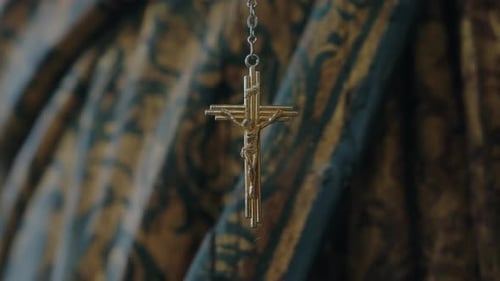 gold crucifix pendant hanging against ornate fabric