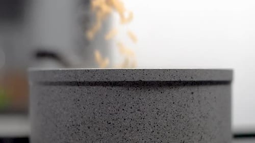 Slow motion macaroni pasta noodles poured into rock non stick pot in kitchen