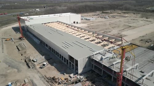 Drone shot of a large warehouse being built, showing structural work and surrounding industrial area