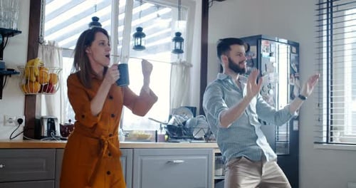 Glücklicher junger, fröhlicher kaukasischer Mann und Frau tanzen morgens beim Frühstück in der modernen Küche