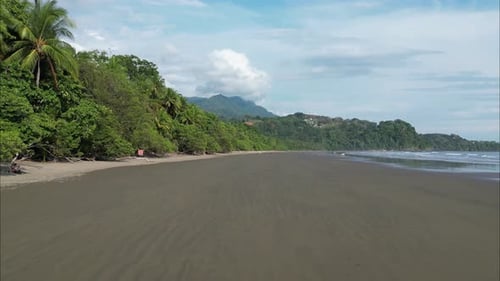 Flying close to the wet sand in Costa Rica beach during low tide with mountains in the background