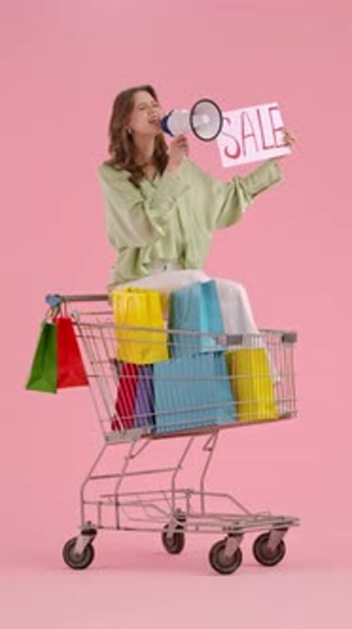 Woman Sitting on Shopping Cart Announcing Sale