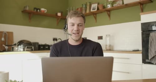 Man with Headset Working on Laptop in Kitchen