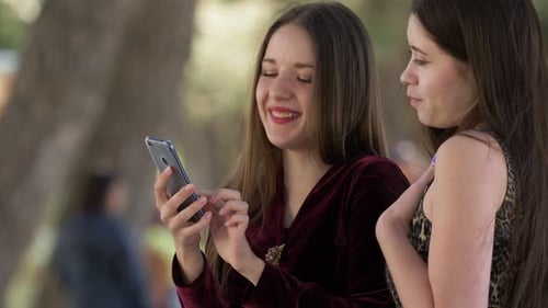 Smiling Women Looking at Phone Together Outdoors