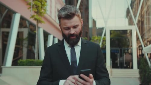 Homem de negócios de sucesso do Smile usa smartphone enquanto caminha na rua do distrito comercial da cidade grande