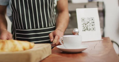 Video of midsection of diverse male seller in coffee shop and customer paying by smartphone