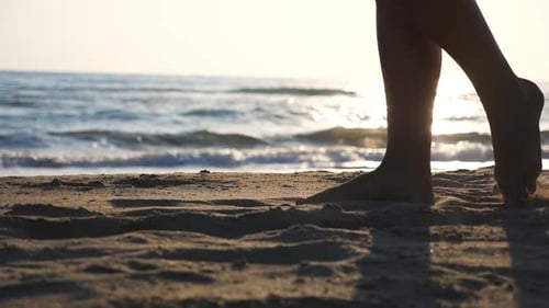Close Up of Female Feet Walking on Golden Sand at the Beach with Ocean Waves at Background