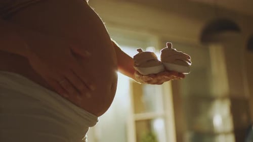 Pregnant Woman Holds Baby Shoes in Golden Light