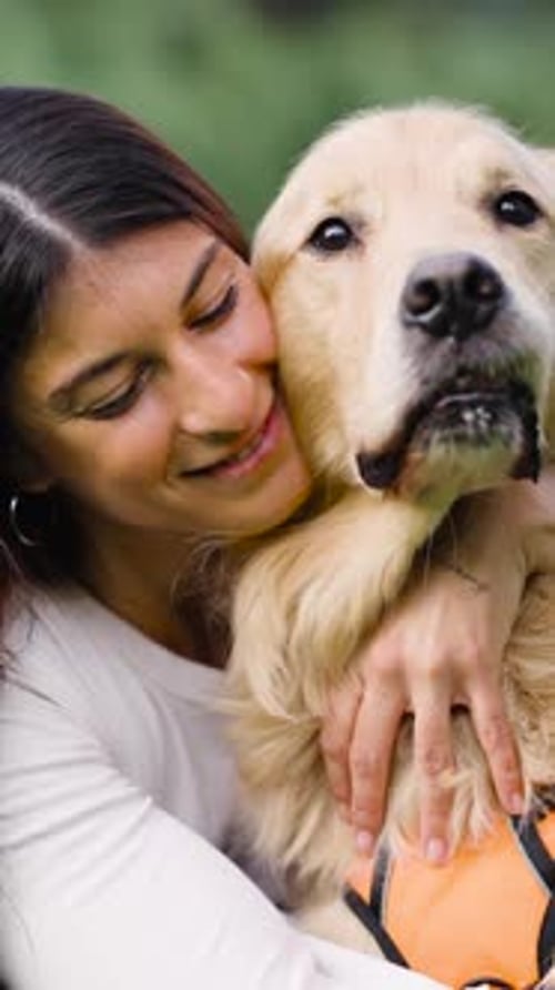 Woman Hugs Golden Retriever Dog Outdoors in Green Setting