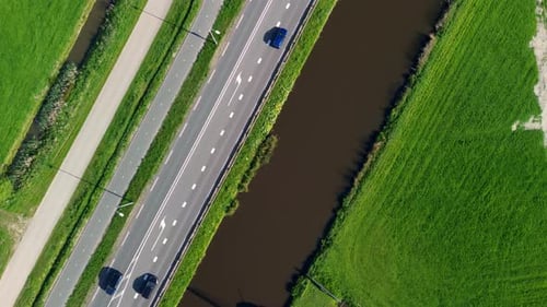 Aerial view of a Dutch countryside with a traditional windmill by a canal, green fields, and road