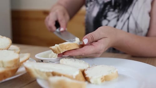 Woman Spreads Cream Cheese on Sliced Bread at Table