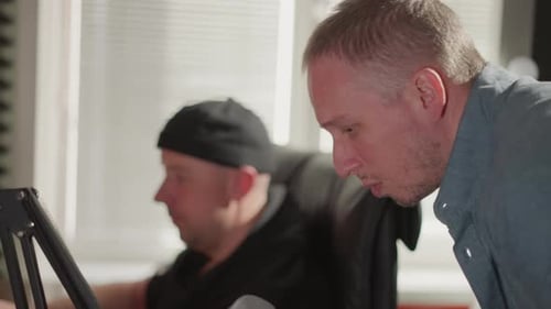 Gros plan d'un homme chantant en studio pendant que le producteur travaille sur ordinateur