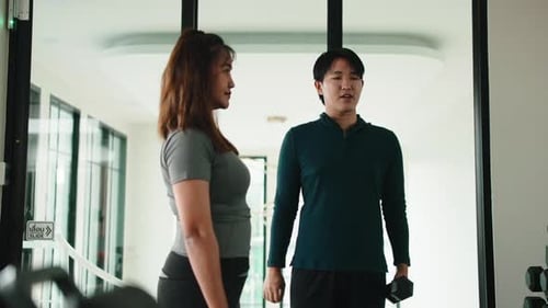Personal Trainer Teaching Woman Front Dumbbell Raise Exercise in Gym