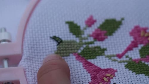 Super close up footage of a lady doing a cross stitch with a needle