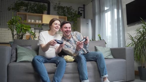 Happy Couple Playing Video Game at Home on Sofa