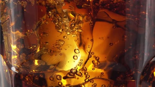 Close up to ice in a glass of cola, bubbles of carbon dioxide slowly rise up.
