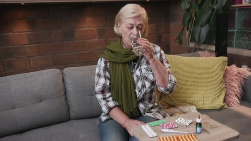 Senior Woman Sitting on Couch Taking Medicine