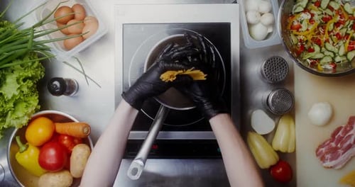 Chef with black gloves adding pasta in a pot of water on the stove, top view