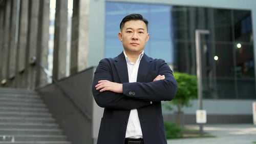Portrait of a confident asian businessman in formal suit standing on street near office building. Se