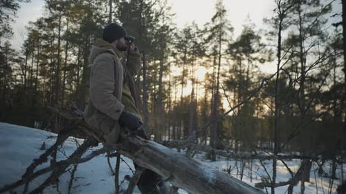 Man with Binoculars Sits on Fallen Tree in Winter