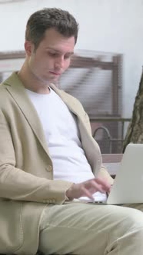 Man Using Laptop Outside While Sitting on Bench