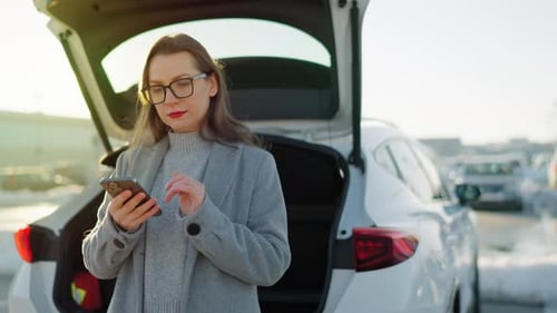 Auburn-Haired Woman Looks at Phone Near Car