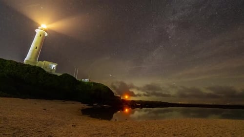Lighthouse Illuminating Coastal Beach at Night Under Stars