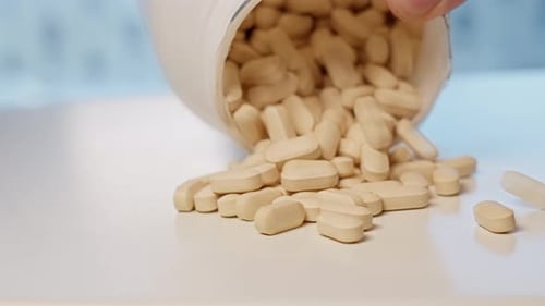 Vitamin C tablets poured out of bottle onto table, close up slow motion